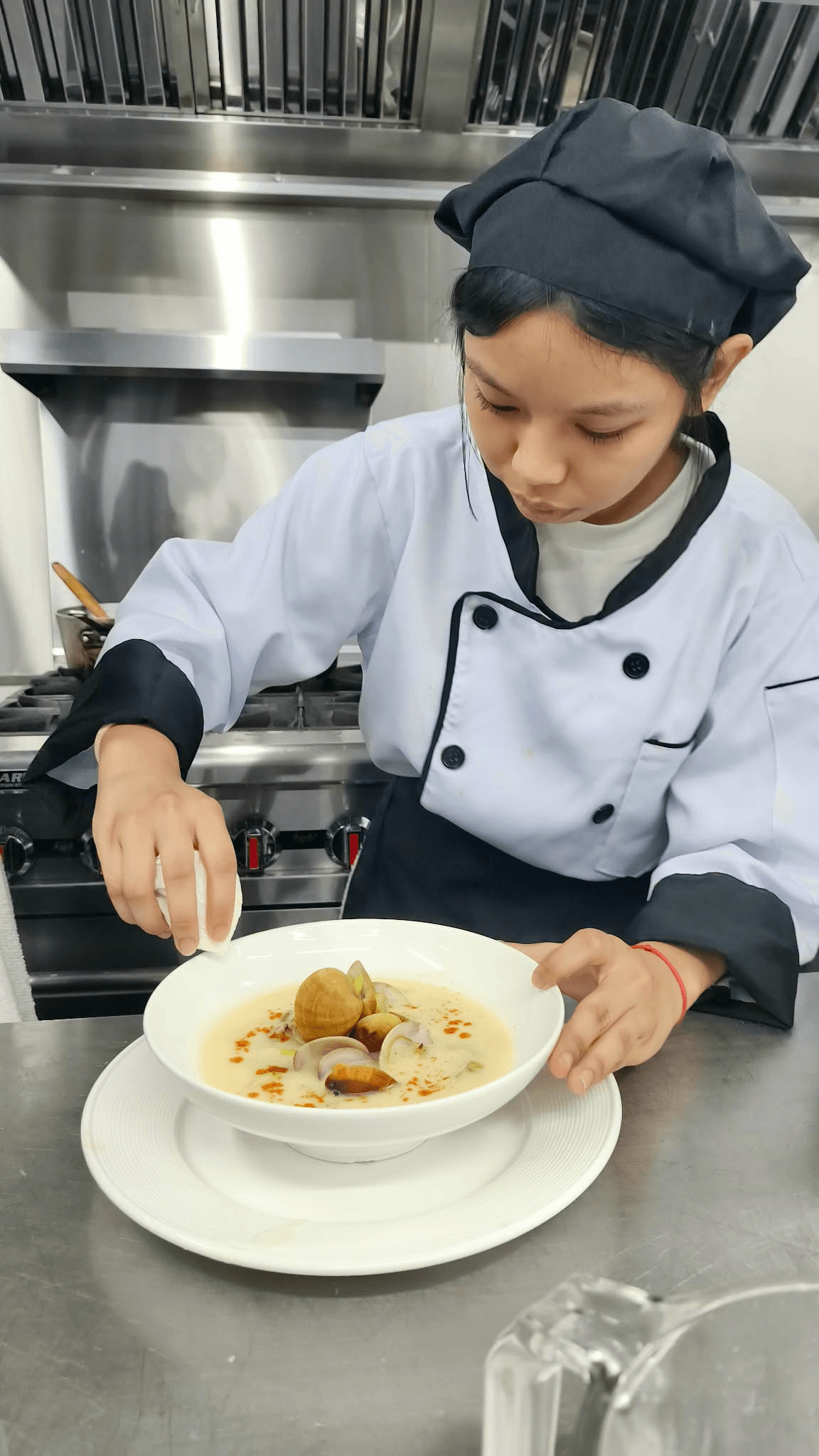 A chef finishing a bowl of clam soup in a professional kitchen